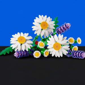 [built-blue-black] A set of building-block style flowers arranged on a black surface against a bright blue background. The bouquet includes large white daisies with yellow centers, smaller white daisies, purple lavender-like spikes, green leaves, and a small red ladybug.