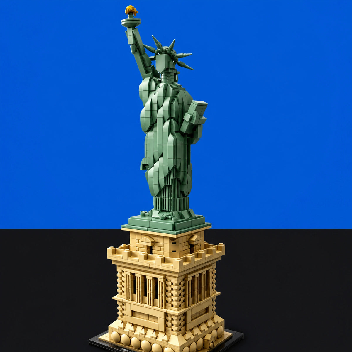 [built-blue-black] A building block model of the Statue of Liberty on a detailed pedestal base, photographed against a split blue and black studio background.
