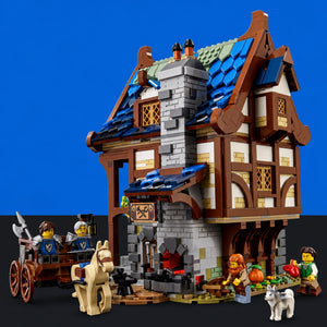 [built-blue-black] A detailed LEGO medieval-style building set with a two-story stone and timber house, blue roof tiles, a fireplace, a cart with minifigures, a horse, and small accessory figures, photographed against a blue and black background.