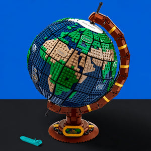 [built-blue-black] A LEGO Earth globe model on a stand, shown against a split blue and black background. The globe features green and beige landmasses, blue oceans, and a brown arm and base.