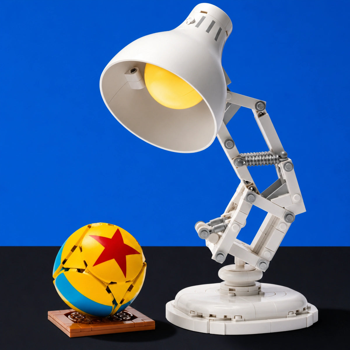 [built-blue-black] A white articulated desk lamp resembling Disney's Woody's lamp, shown lit against a blue background, next to a yellow and blue ball with a red star on a wooden base.