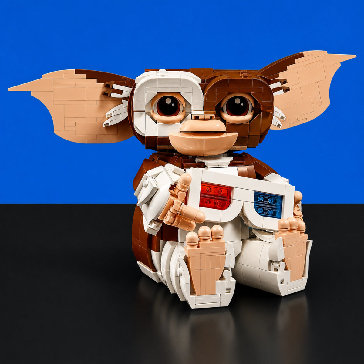 [built-blue-black] A toy building-block character resembling a gremlin or goblin, posed sitting against a split blue and black background. The figure has large dark eyes, tan and brown coloring, and white body panels with small red and blue details.