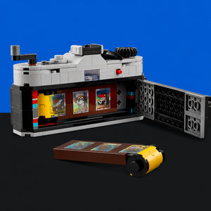 [built-blue-black] A LEGO-style model set displayed on a black surface against a bright blue background, featuring a gray, black, and white structure with colorful panel details and a separate brown-and-yellow accessory piece placed in front.