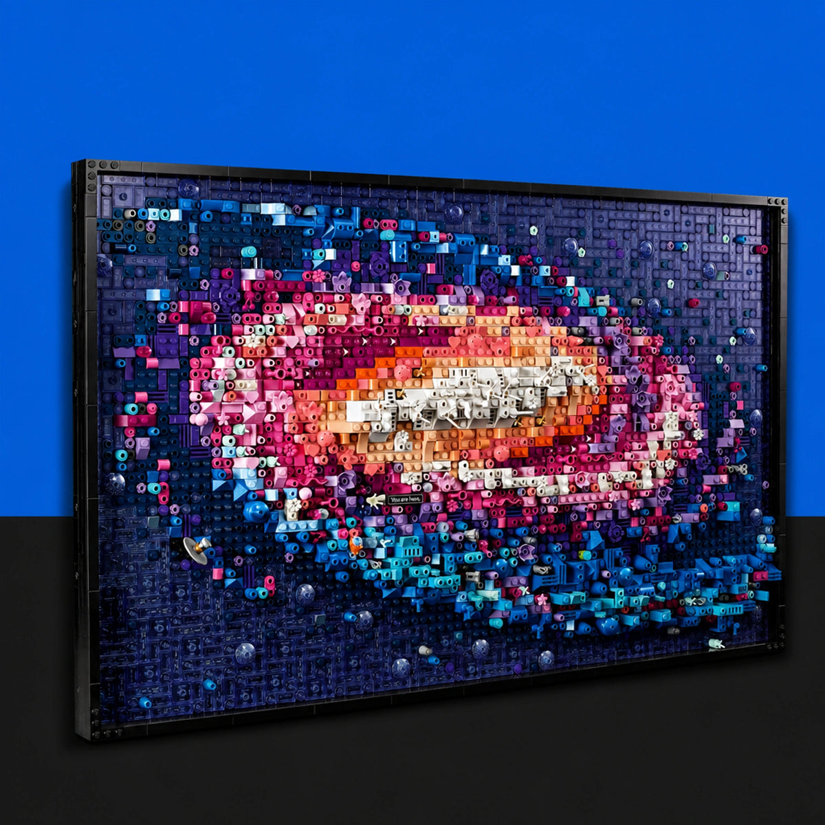 [built-blue-black] A framed wall art piece made of many colorful 3D letters and numbers, forming a galaxy or nebula design, shown against a blue and black background.