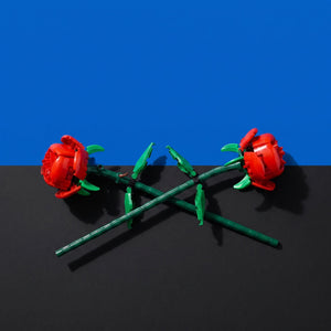 [built-blue-black] Two red rose-shaped items with green stems and leaves, arranged crossed on a black surface against a blue background.