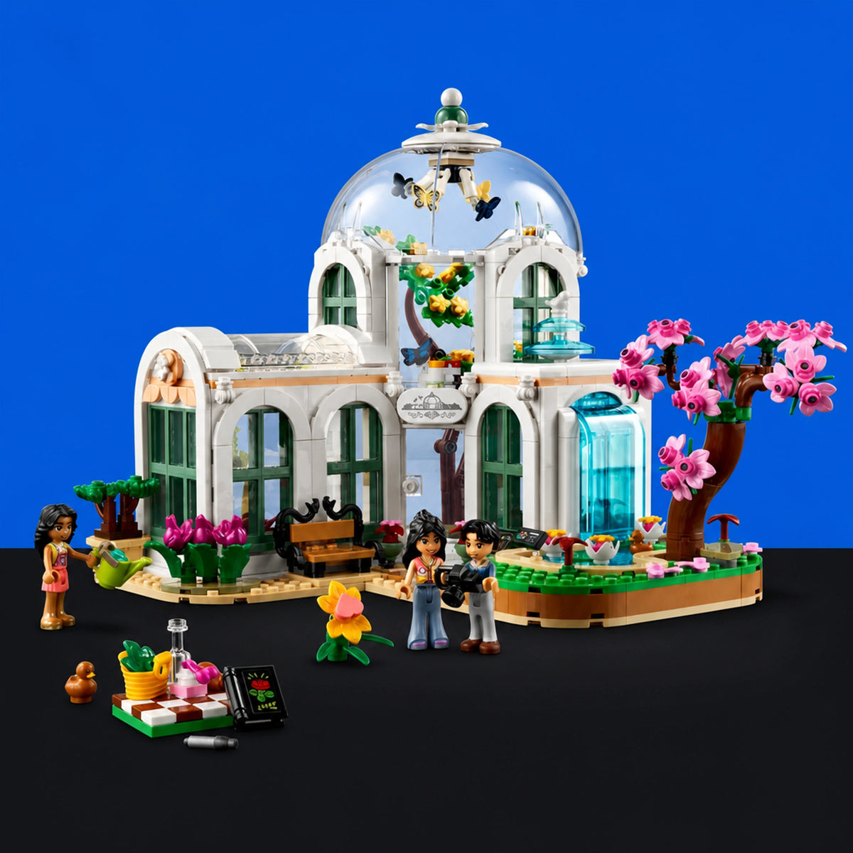 [built-blue-black] LEGO City Garden House set with white building, clear glass dome, green windows, pink cherry blossom tree, butterfly dome, and small minifigures on a black surface against a blue background.