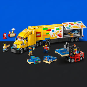 [built-blue-black] LEGO City Transport set with a yellow semi-truck carrying colorful building blocks, plus several minifigures and a red forklift on a black surface against a blue background.