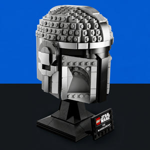 [built-blue-black] A LEGO Star Wars The Mandalorian helmet bust model on a black display stand, with a small branded plaque, set against a split blue and black background.