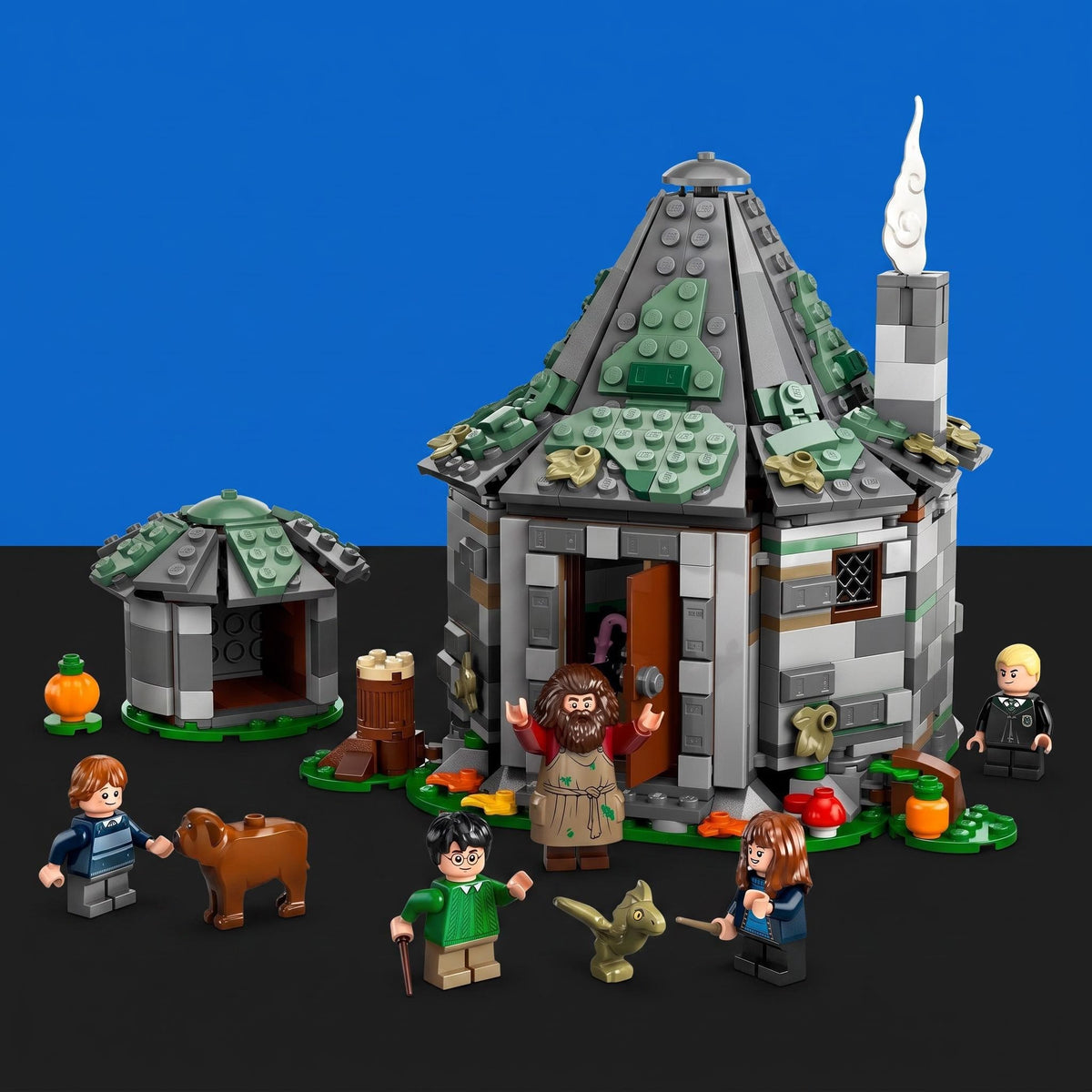 [built-blue-black] A LEGO Harry Potter Hogwarts castle building set displayed on a black surface against a blue background, with minifigures, a small pumpkin, a dog, and other themed accessories arranged around the structure.