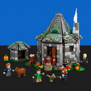[built-blue-black] A LEGO Harry Potter Hogwarts castle building set displayed on a black surface against a blue background, with minifigures, a small pumpkin, a dog, and other themed accessories arranged around the structure.