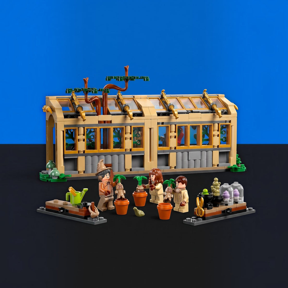 [built-blue-black] A LEGO building set featuring a greenhouse structure with several small minifigures and gardening accessories arranged in front, photographed on a blue and black studio background.